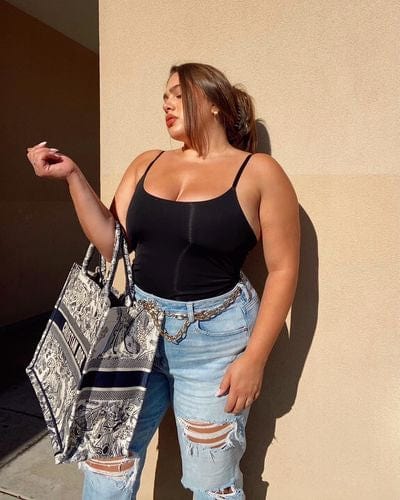 Woman in black top and jeans holding tote bag.