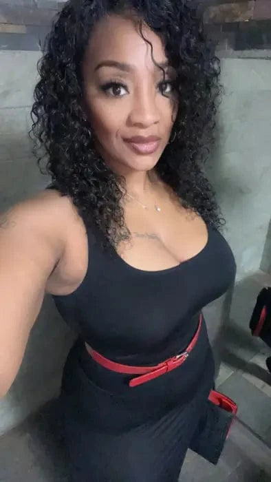 Woman with curly hair wearing a black top and red belt.