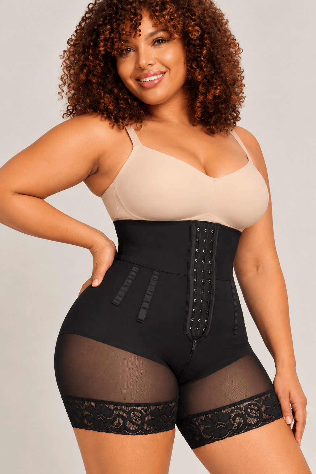A plus-size model wearing a black high-waisted shapewear brief with sheer mesh and lace trim, paired with a beige bra, against a light gray studio background. 9 BONED SCULPT SHAPEWEAR SHORTS 