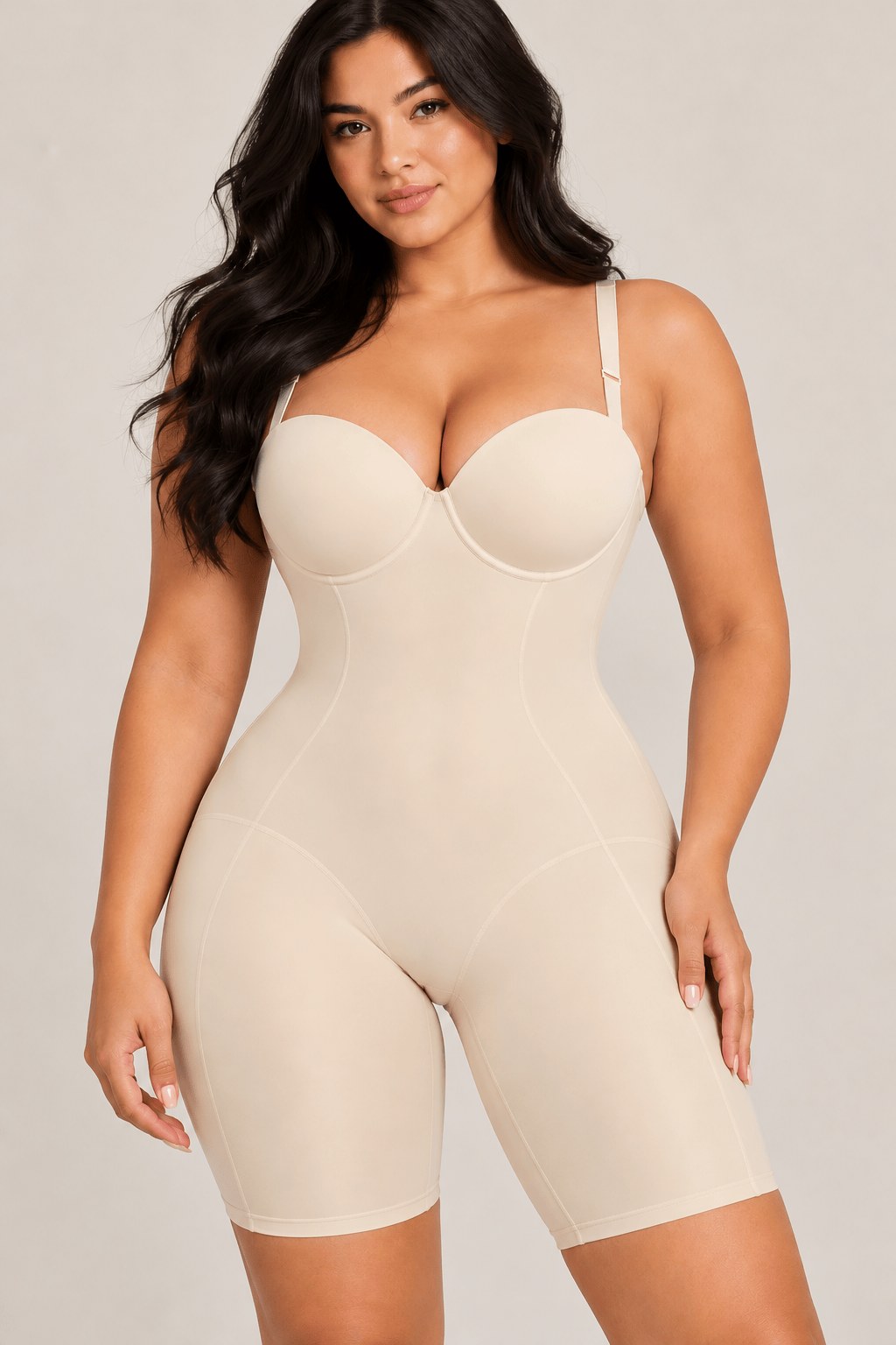 A plus-size model wearing a beige Strapless Cupped compression bodysuit with a bustier neckline and built-in shapewear shorts, photographed against a solid light gray studio background.