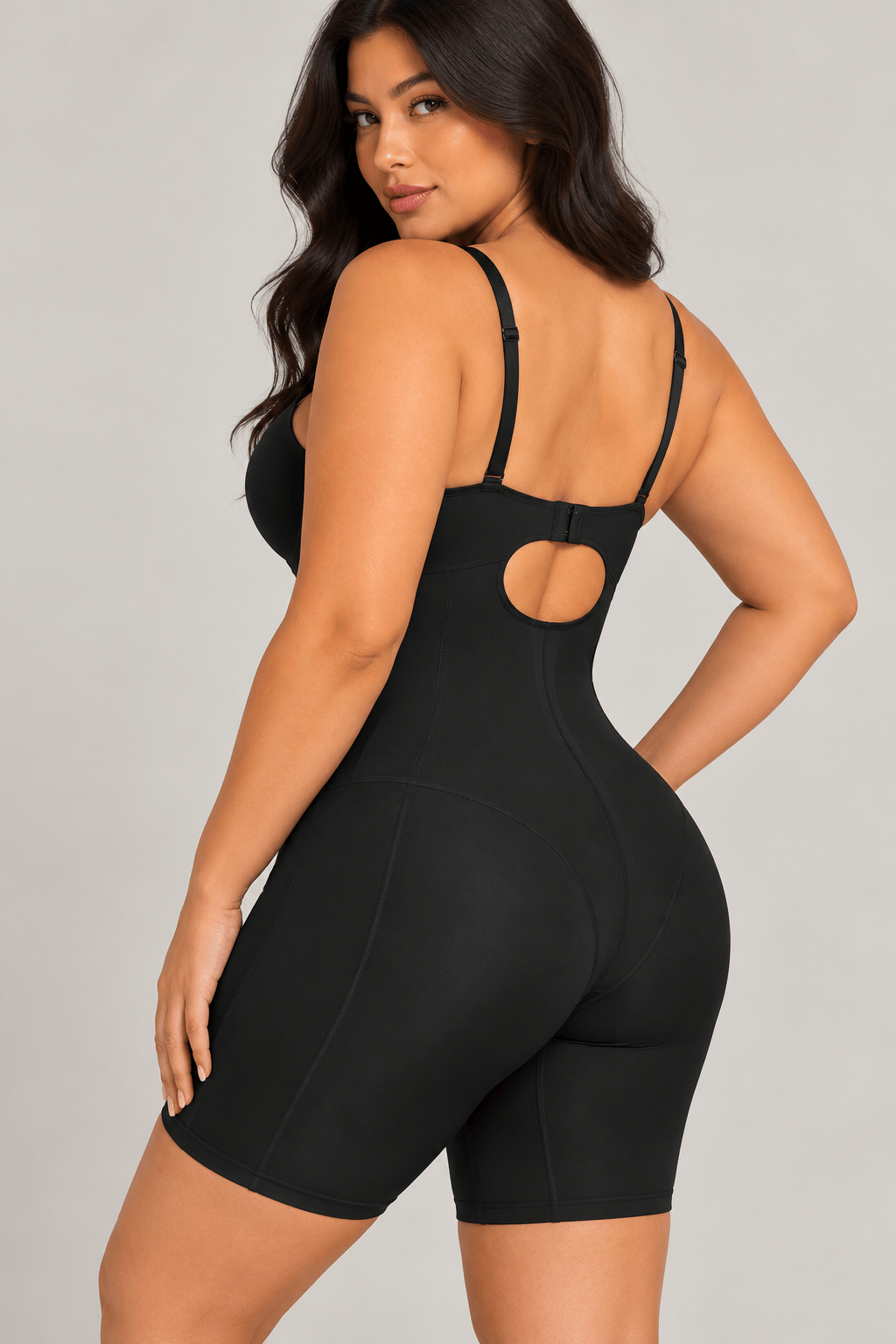 A woman modeling a black Cupped strapless mid thigh shaping shapewear bodysuit shown from a three-quarters back view against a light gray studio background.