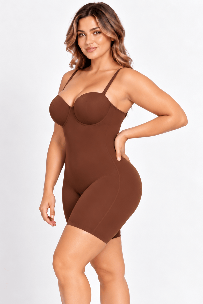 A woman modeling a brown shapewear bodysuit with a bustier-style upper section and fitted shorts, photographed against a clean white studio background.