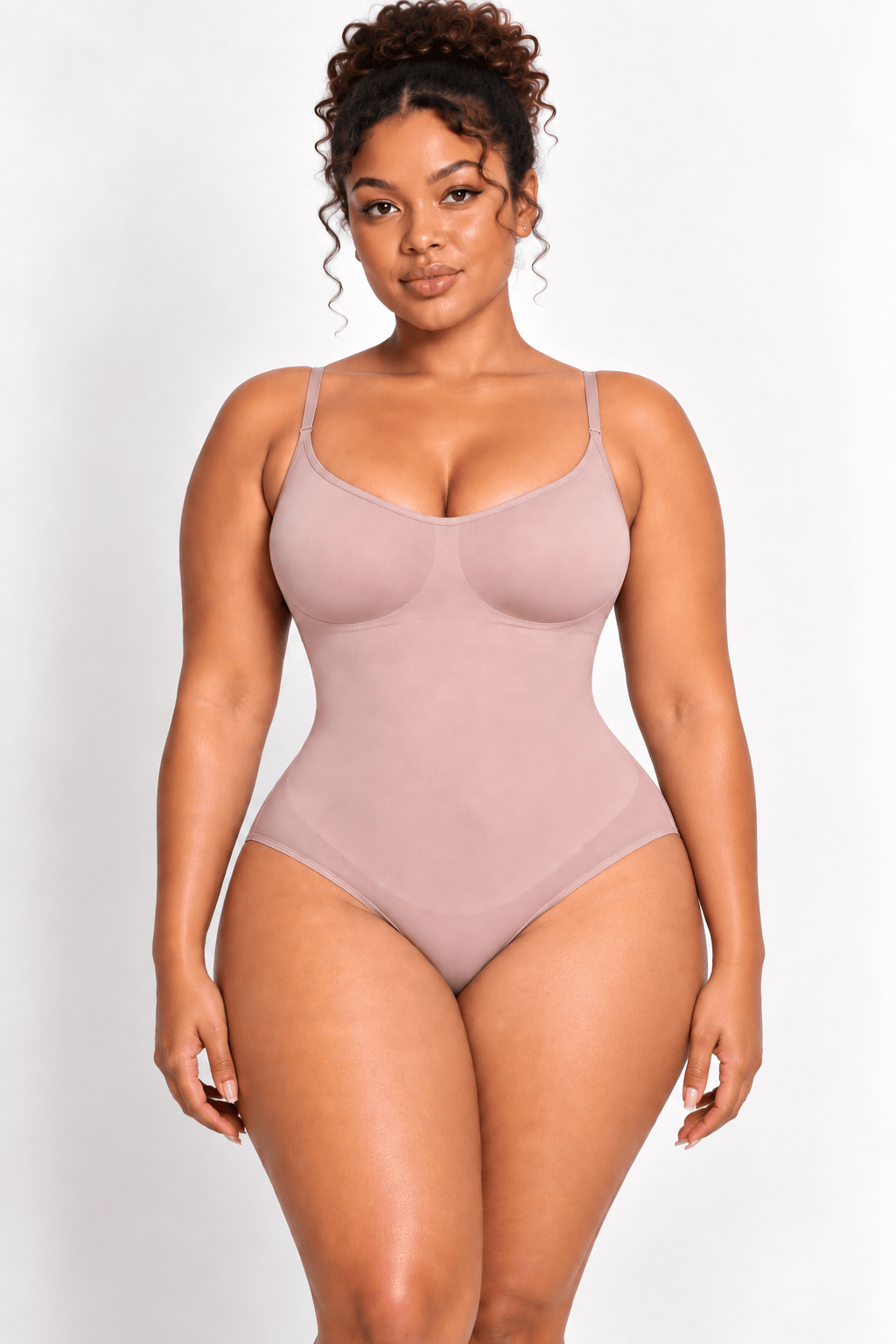 A woman modeling a light pink seamless bodysuit against a plain light gray studio background.