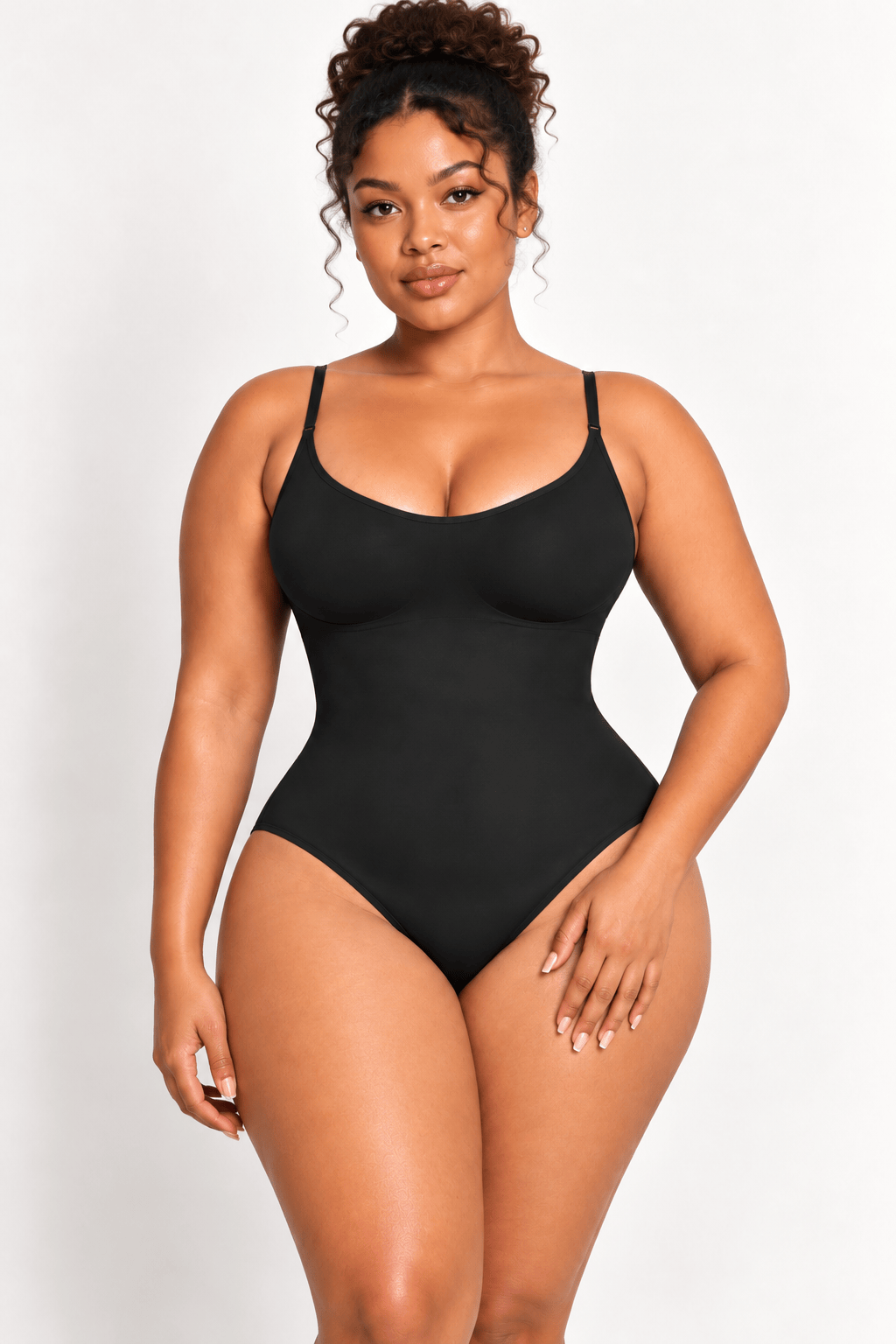 A woman modeling a black, sleeveless, high-cut bodysuit or shapewear unitard against a plain light gray studio background.